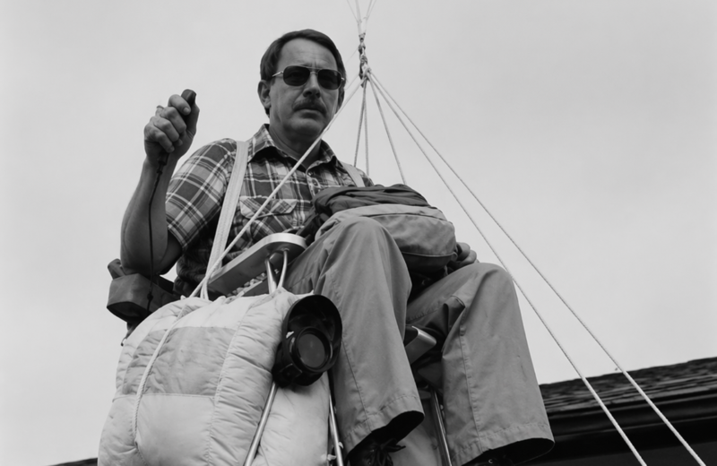 Larry Walters elevándose en una silla de jardín sostenida por globos sobre una casa.