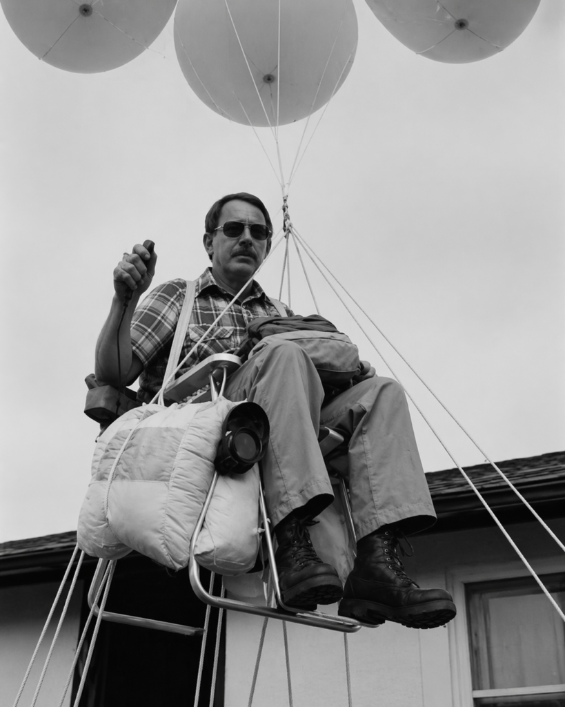 Larry Walters elevándose en una silla de jardín sostenida por globos sobre una casa.